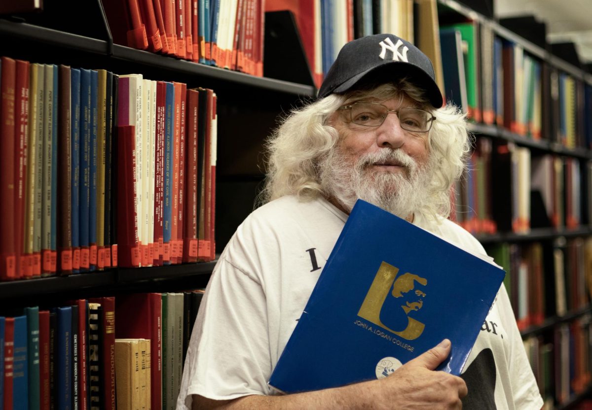 John A. Logan College English instructor Kenneth Gilbert stands among the shelves in the Learning Resources Center. Gilbert, who has taught at Logan since 1994, is also a poet, tennis player, and lifelong fan of rock ’n’ roll.