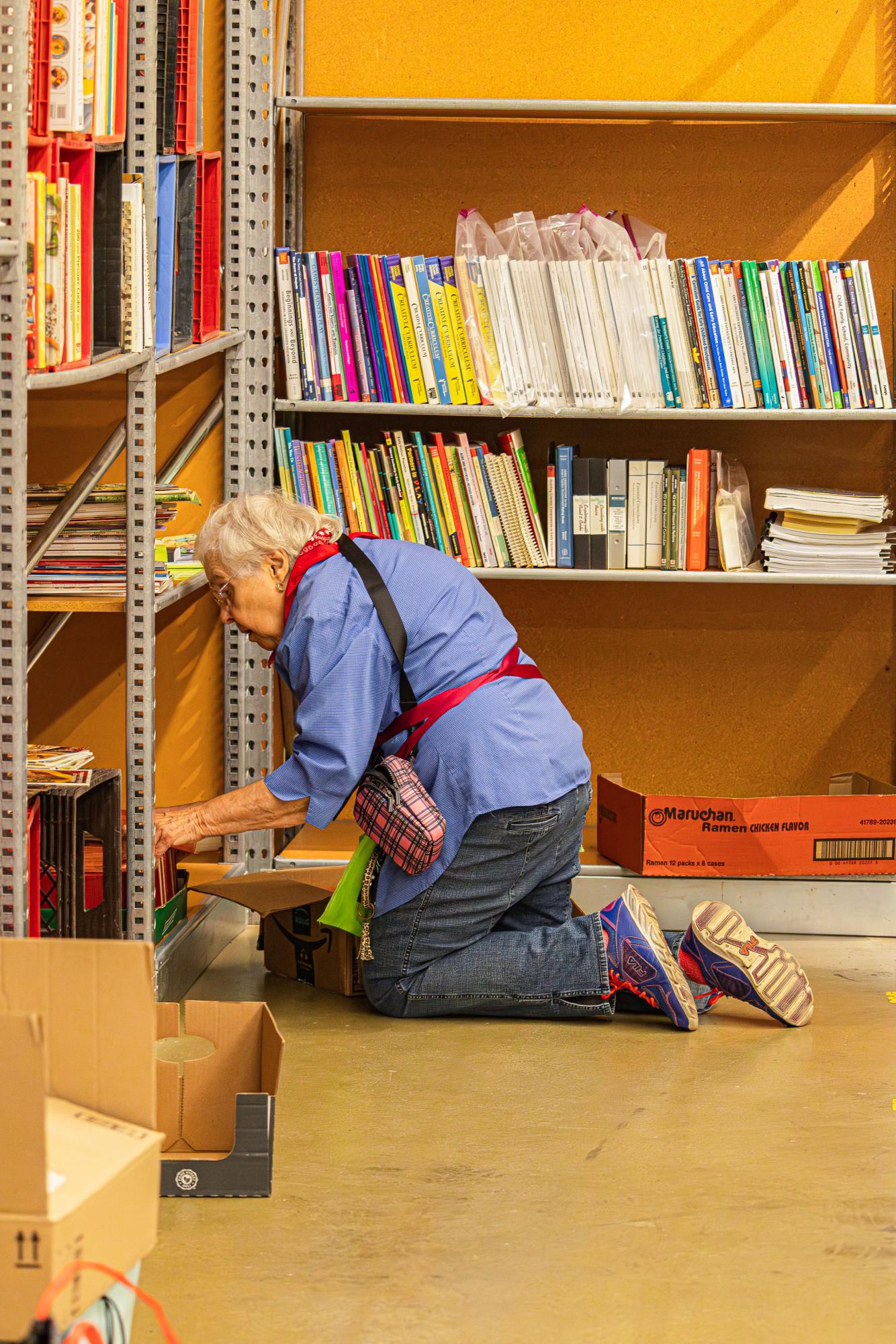 A volunteer kneels to sort books on a shelf during preparations for the Carbondale Hunger Sale at University Mall in Carbondale Tuesday, April 28, 2026.